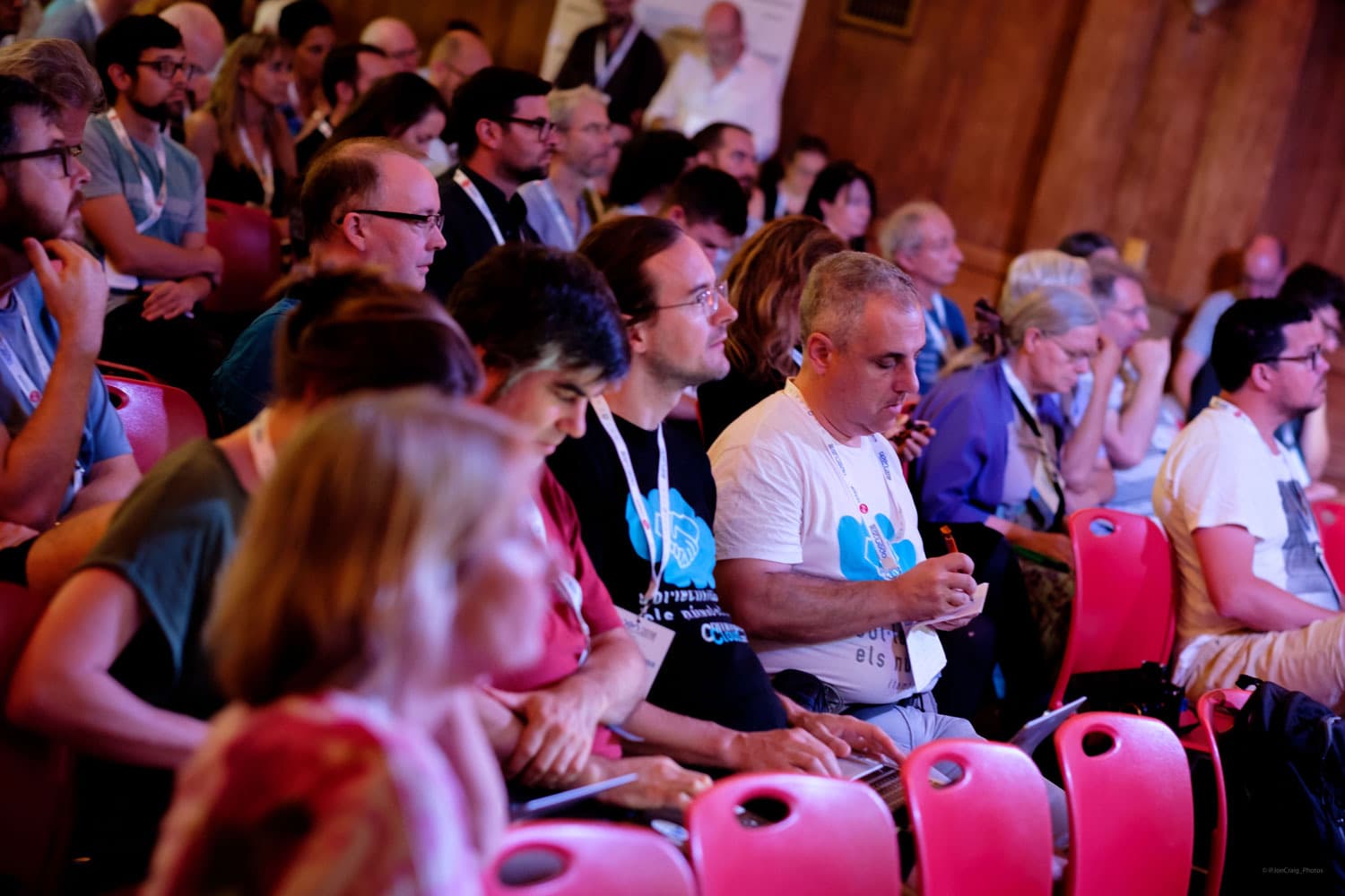 An audience listening at a conference, some taking notes