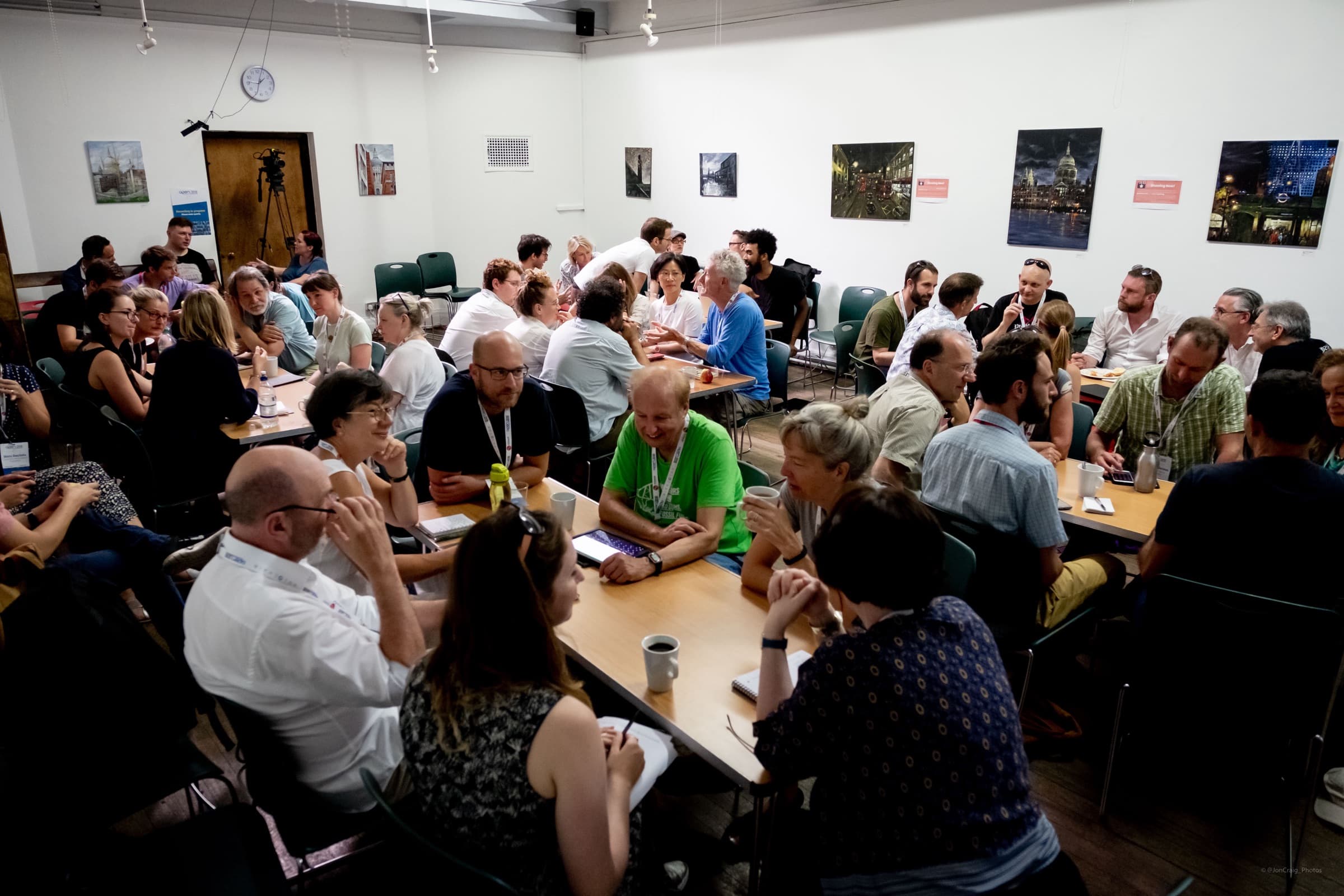A busy room of people in conversation around tables at a workshop