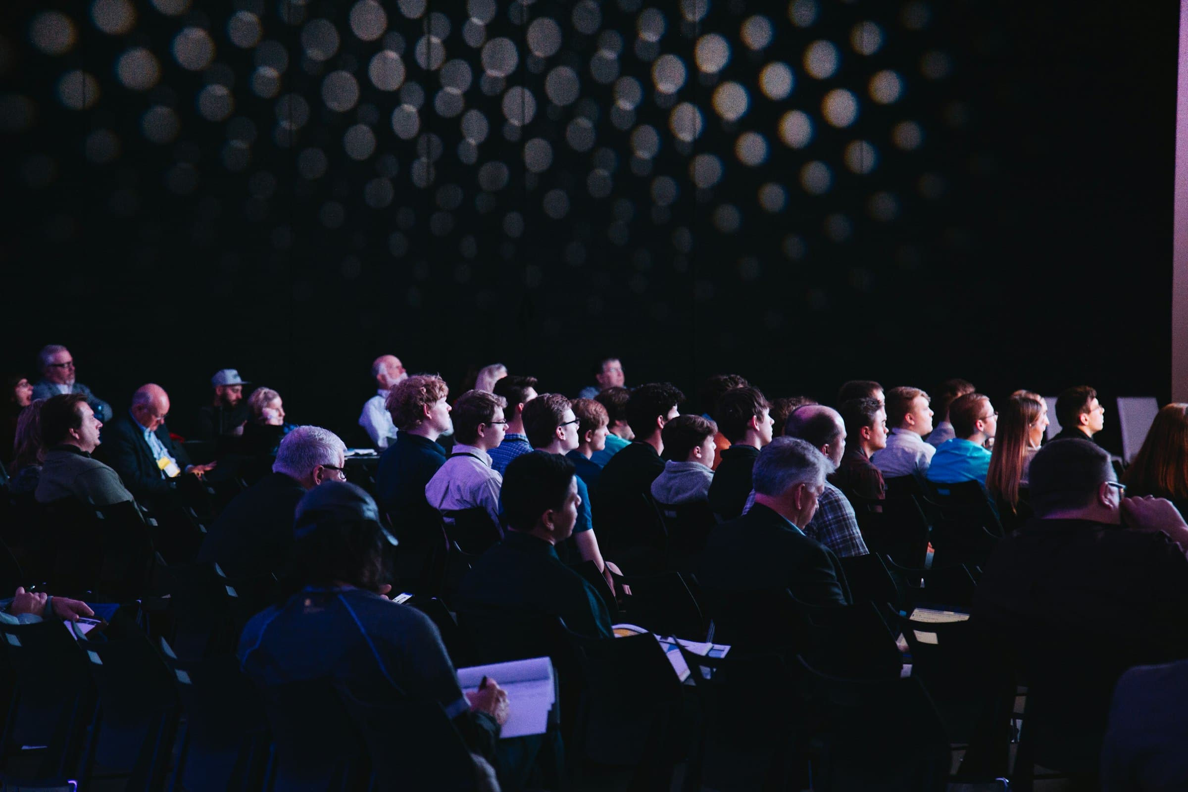 An audience seated in a darkened conference hall